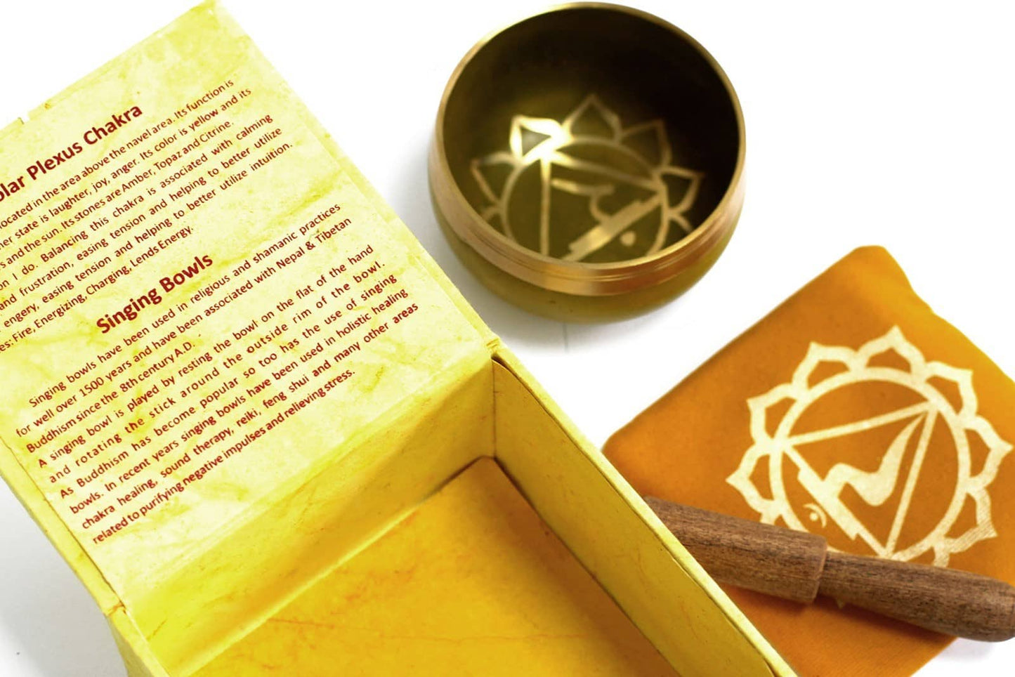 Coffret ouvert jaune contenant un bol tibétain jaune avec une bordure dorée. À l'intérieur, le symbole du Chakra Plexus Solaire doré. À côté, un tapis jaune avec le symbole du Chakra Plexus Solaire doré, et un fuseau en bois.