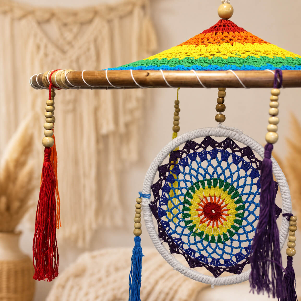 Vue rapprochée du parasol crocheté arc-en-ciel sur structure en bambou avec perles et pompons.
