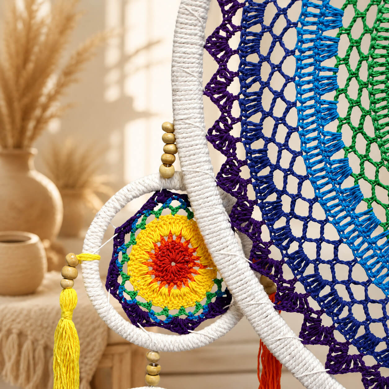 Détail d'un cercle satellite avec mandala crocheté arc-en-ciel et pompon jaune perles en bois.