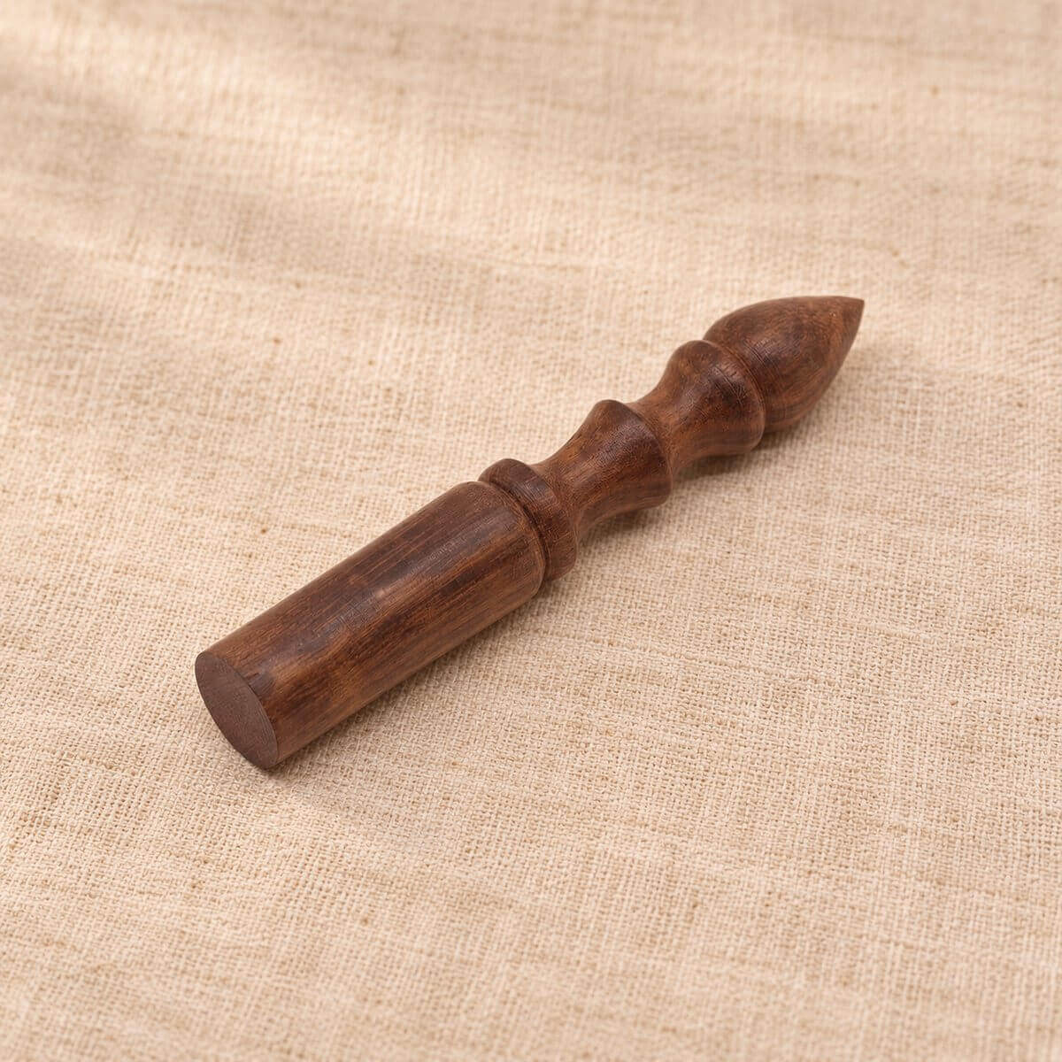 Petit bâton de méditation en bois nu au profil tourné, terminé par une pointe en bouton, posé sur un lin beige