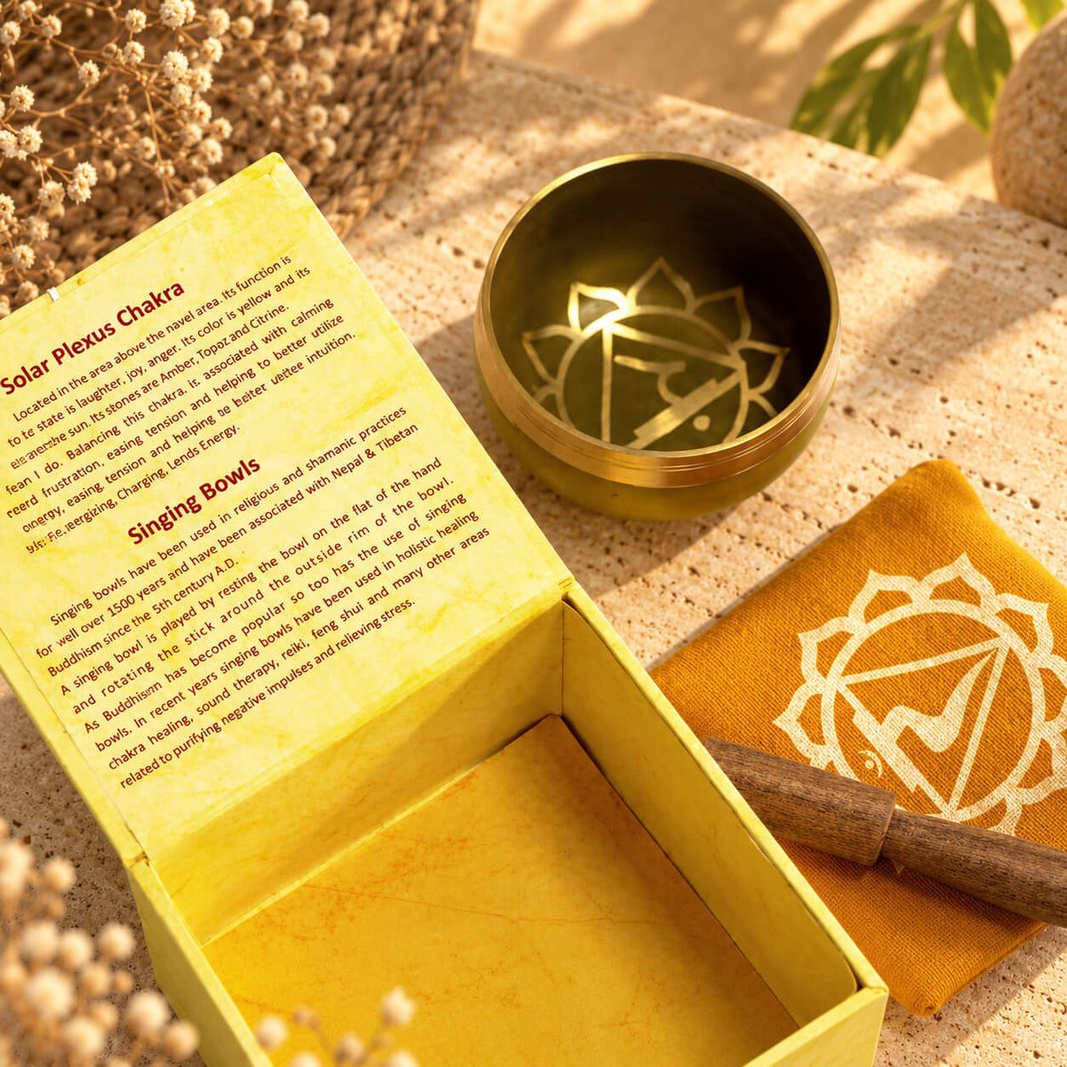 Symbole doré du plexus solaire au fond du bol en laiton, près de la boîte jaune ouverte et du coussin imprimé