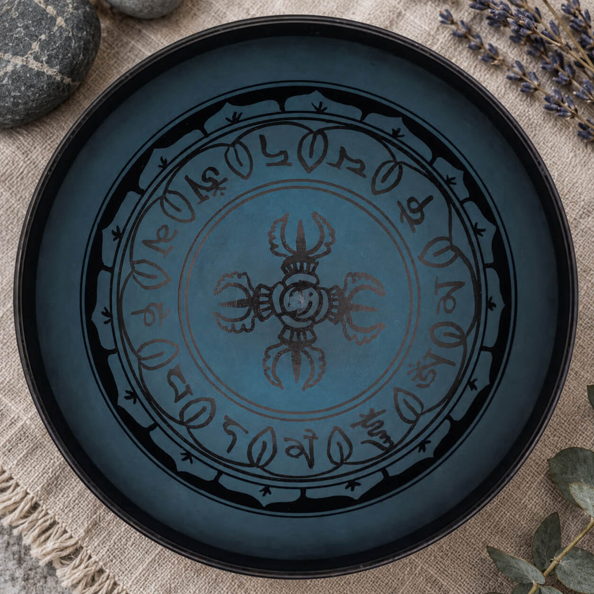 Double dorje noir au centre du bol bleu, entouré d'un anneau de syllabes et de pétales