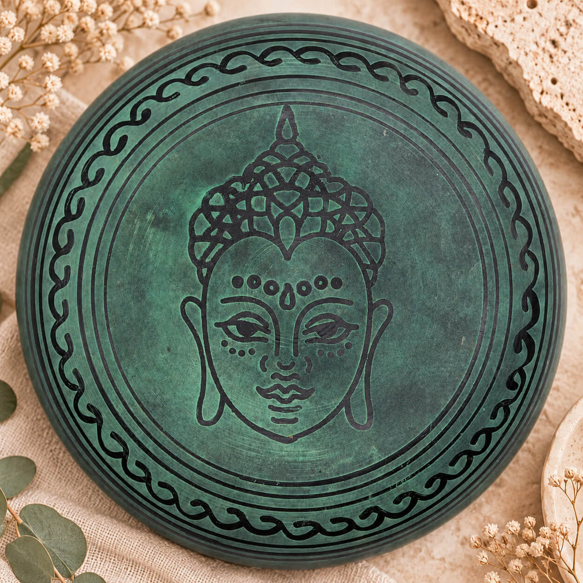 Dessous du bol chantant vert gravé d’un visage de Bouddha cerclé d’une bordure ondulée