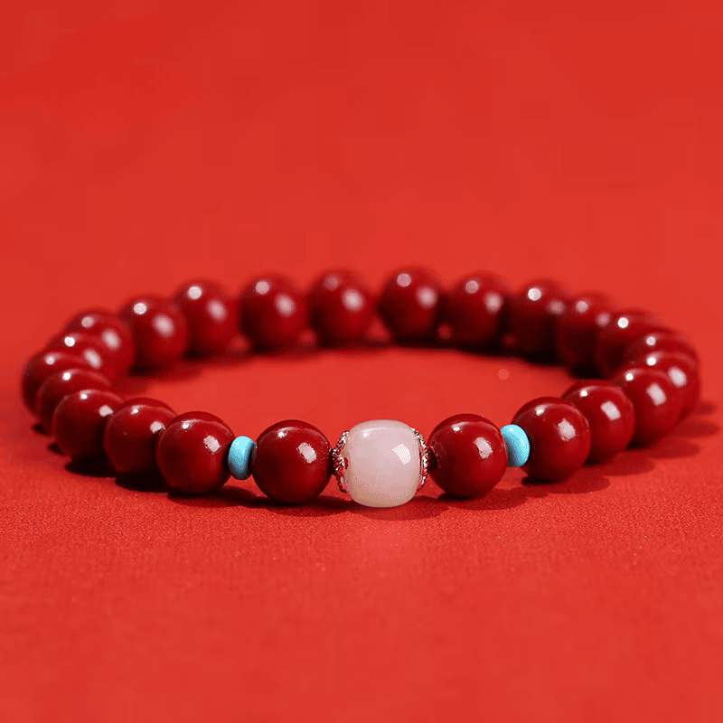 Bracelet en perles de cinabre rouge avec perle centrale en quartz rose et touches turquoise sur fond rouge.