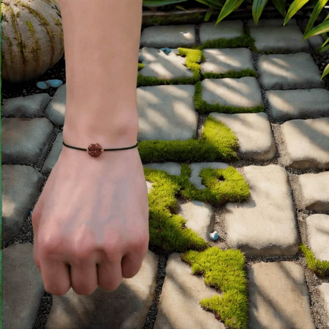 Bracelet porte-bonheur tibétain avec trèfle en cinabre porté au poignet dans un jardin japonais.