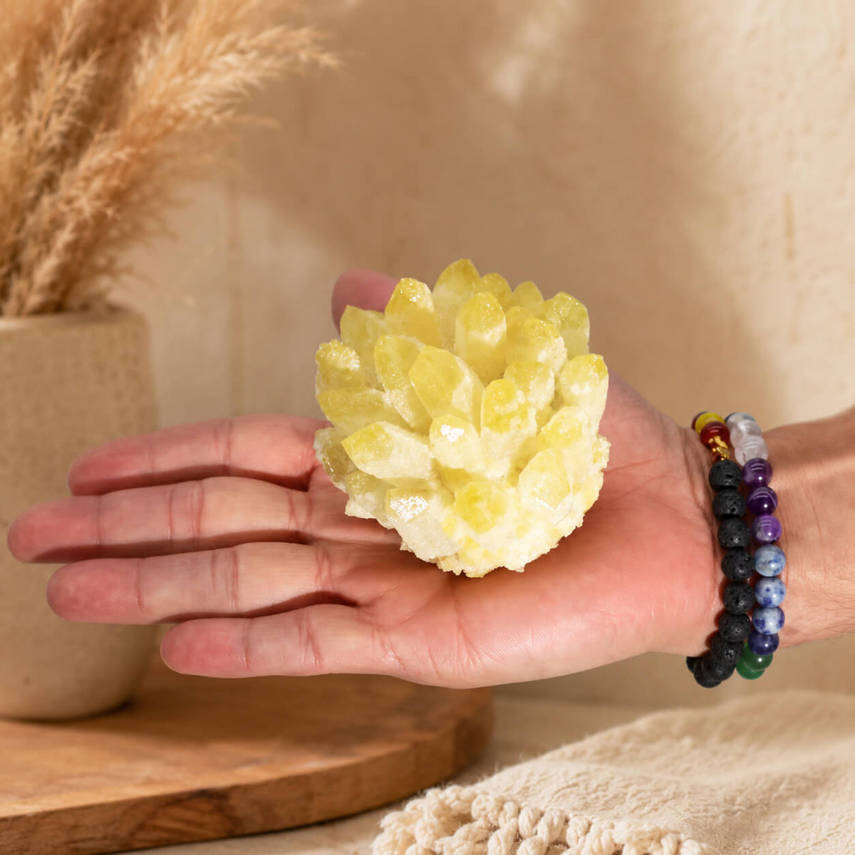 Grappe de quartz jaune fantôme tenue dans une main avec bracelets en pierres naturelles