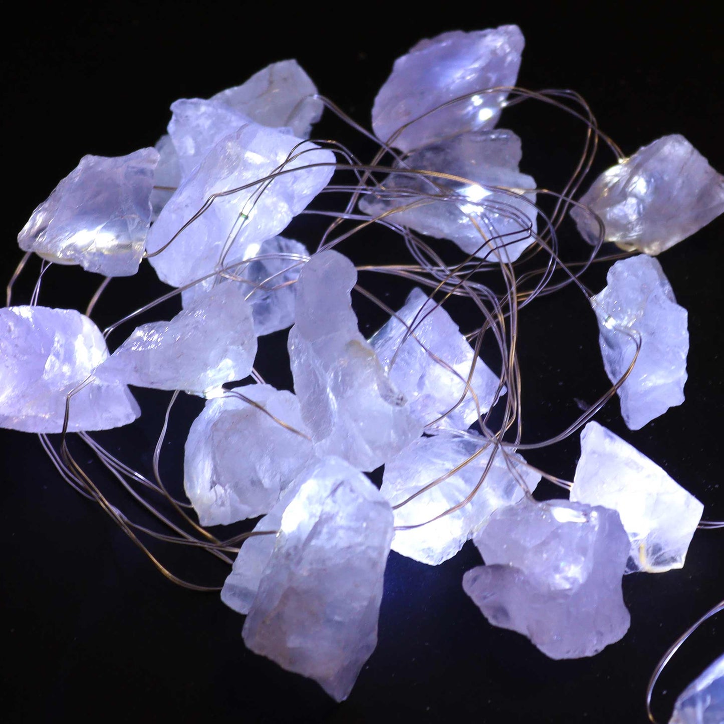 Une guirlande lumineuse allumée en pierres naturelles de quartz blanc sur fond noir.