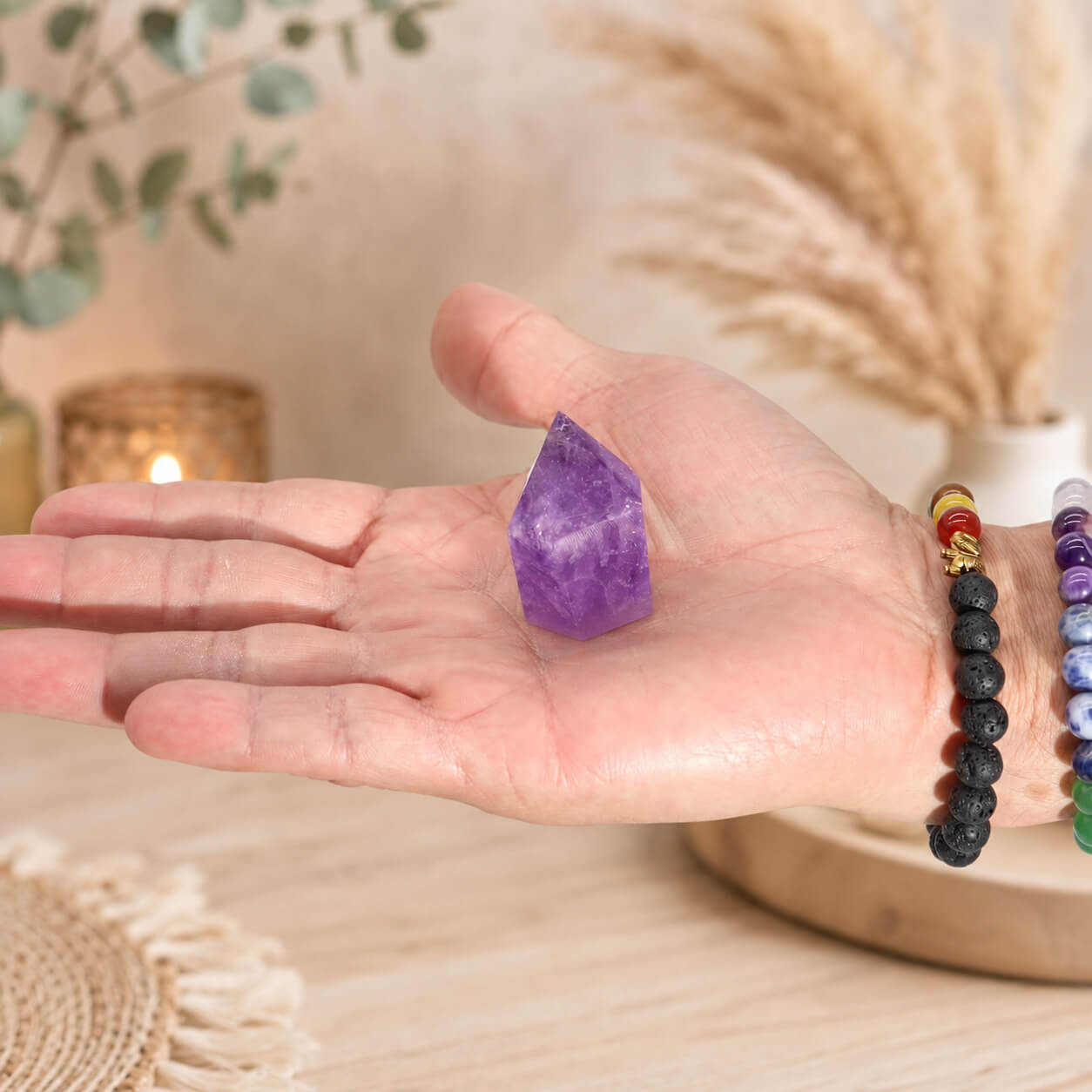 Petite pointe d'améthyste naturelle tenue dans une main avec bracelets en pierres naturelles.