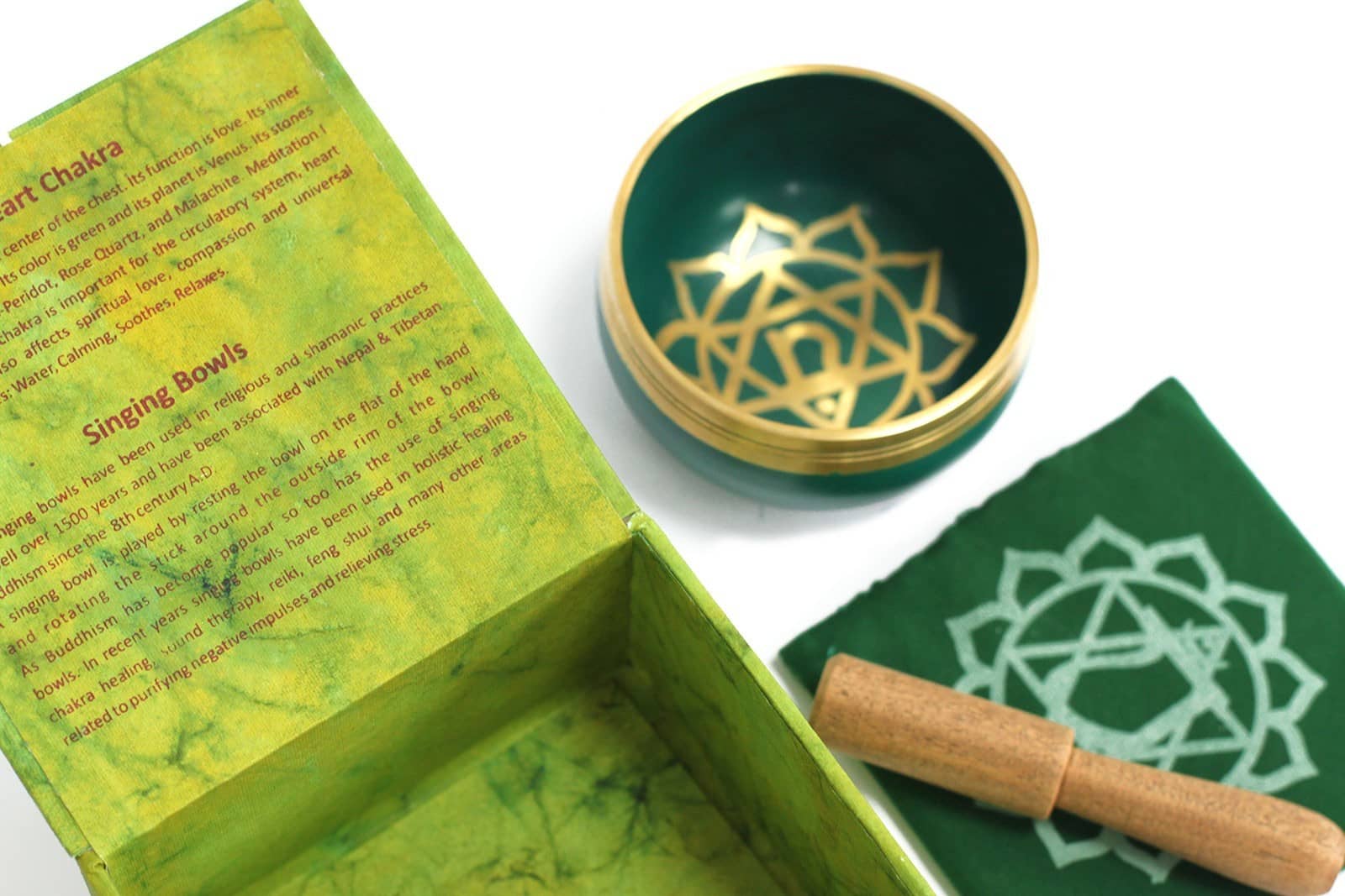 Coffret ouvert vert contenant un bol tibétain vert avec une bordure dorée. À l'intérieur, le symbole du Chakra Cœur doré. À côté, un tapis vert avec le symbole du Chakra Cœur doré, et un fuseau en bois.