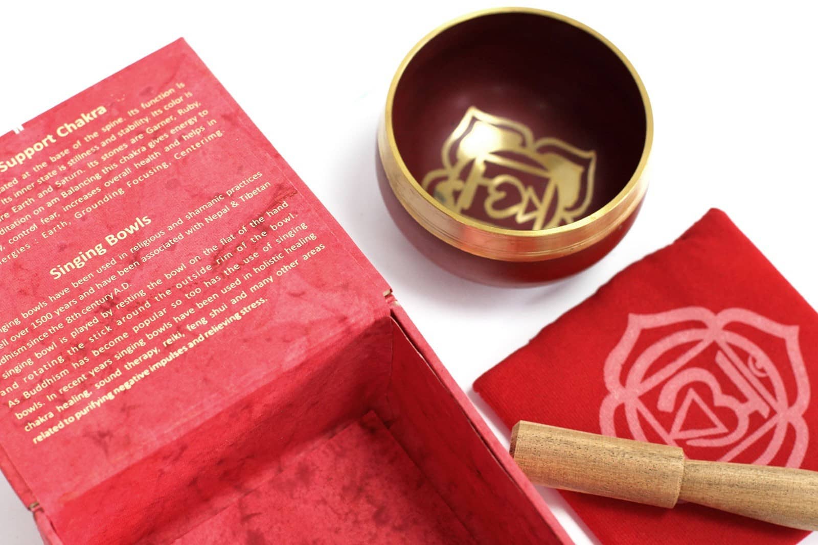 Coffret ouvert rouge contenant un bol tibétain rouge avec une bordure dorée. À l'intérieur, le symbole du Chakra Racine doré. À côté, un tapis rouge avec le symbole du Chakra Racine doré, et un fuseau en bois.