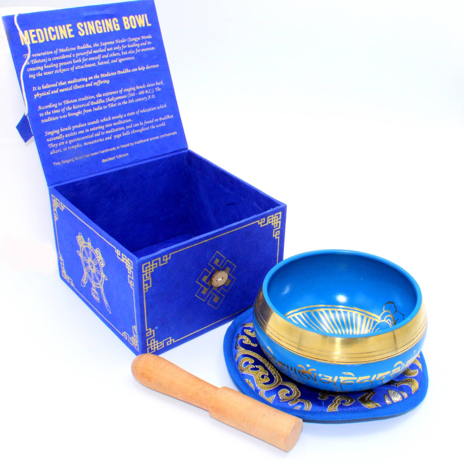 Coffret ouvert bleu contenant un bol tibétain bleu avec un Bouddha Médecine doré à l'intérieur et une bordure dorée. Le bol est posé sur un tapis bleu avec des motifs assortis, et un fuseau en bois est placé à côté.