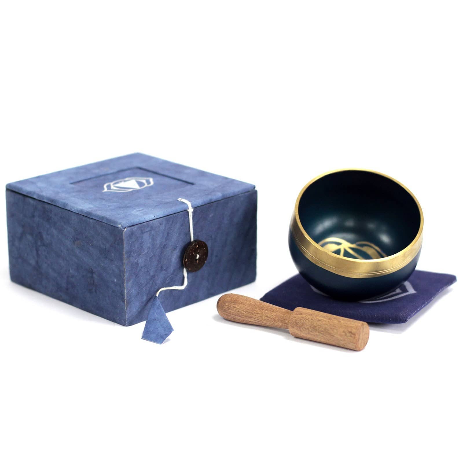 Coffret fermé bleu foncé à côté, un bol tibétain bleu foncé avec une bordure dorée. À l'intérieur, le symbole du Chakra Troisième Œil doré, posé sur un tapis bleu foncé, accompagné d'un fuseau en bois.