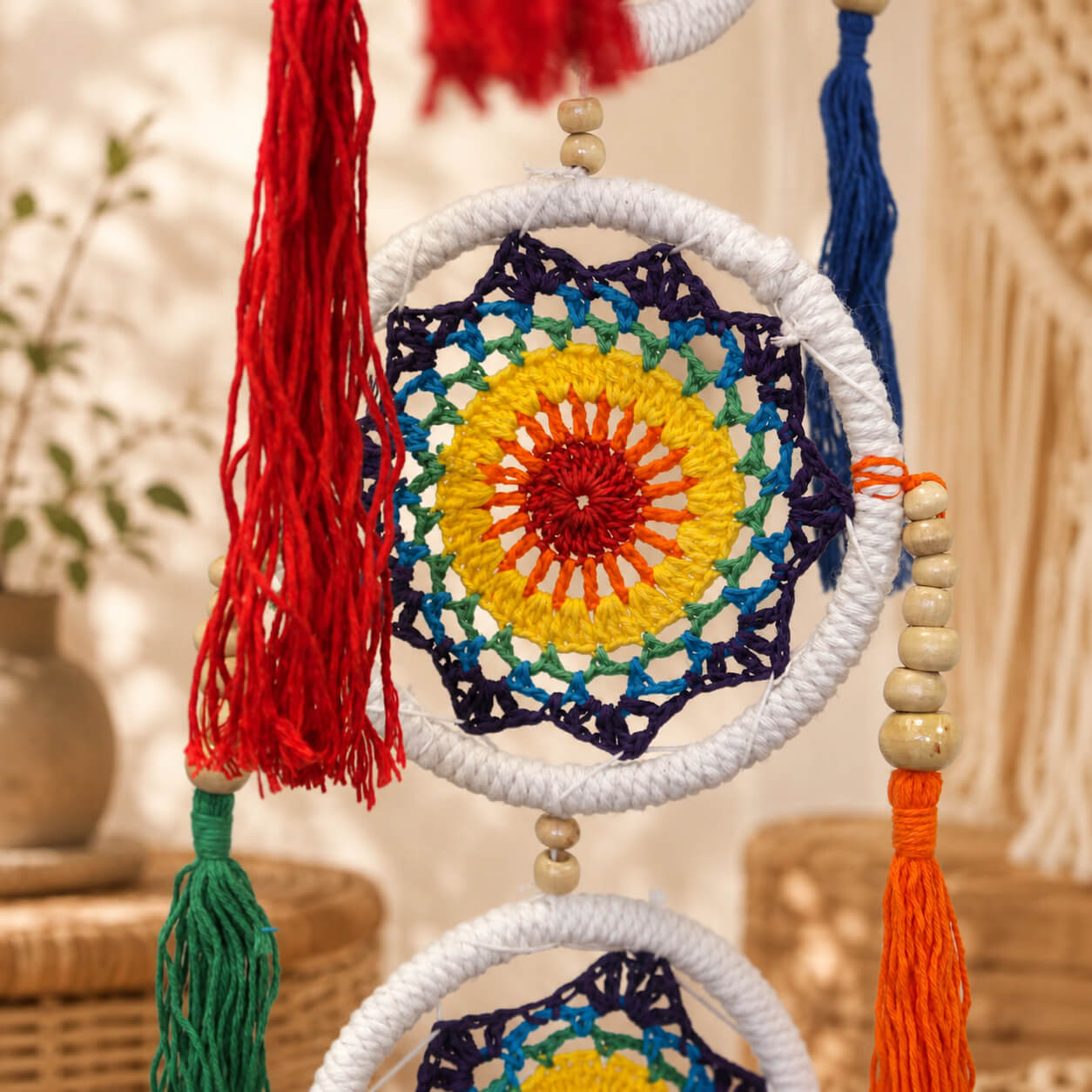 Détail d'un mandala crocheté arc-en-ciel avec pompons rouge orange et perles en bois.