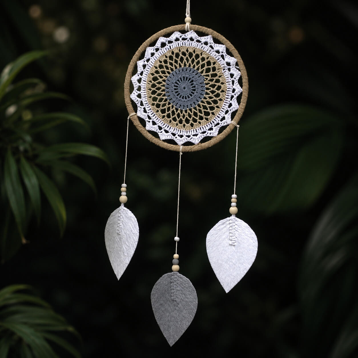 Attrape-rêve rond avec mandala crocheté blanc beige et gris bleuté et trois plumes tissées en forme de feuilles.
