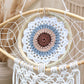 Détail du médaillon crocheté central de l'attrape-rêve avec mandala blanc, bleu, beige et marron sur cerceau en rotin.