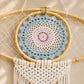 Détail du médaillon crocheté central de l'attrape-rêve avec mandala bleu, blanc et rose pastel sur cerceau en rotin.