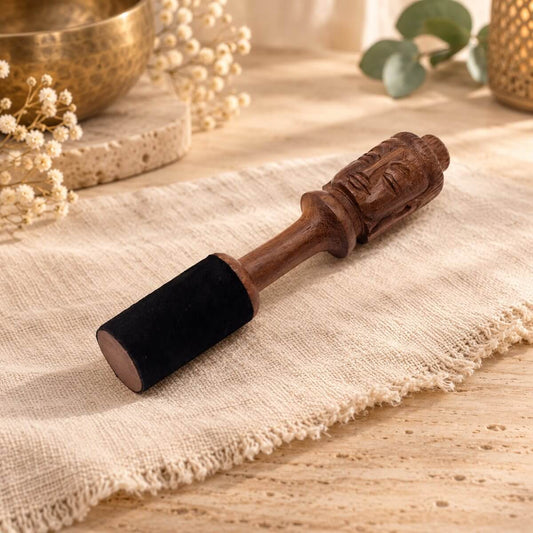 Bâton de méditation en bois sculpté d’un visage de Bouddha, extrémité gainée de noir, posé sur un lin beige près d’un bol chantant doré