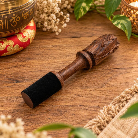 Bâton de méditation en bois sculpté d’une tête d’éléphant, embout noir, posé sur une table en bois devant un bol tibétain sur coussin rouge