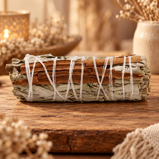 Bâton de sauge blanche avec des lamelles d'écorce de cannelle, lié par une ficelle blanche, posé sur une planche en bois