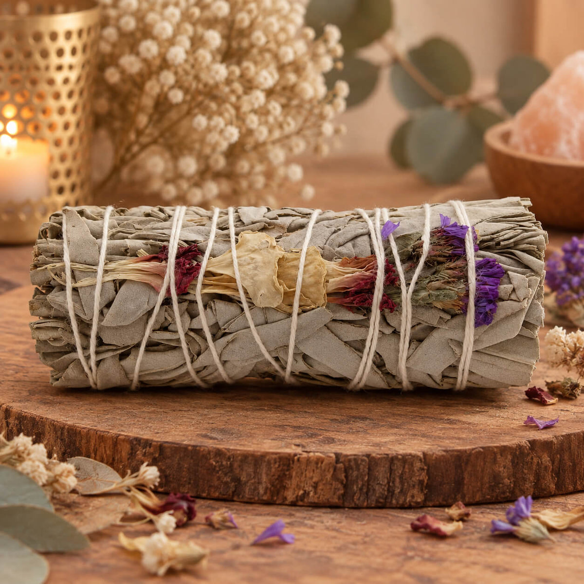 Bâton de sauge blanche orné de fleurs séchées pourpres, crème et violettes, posé sur une rondelle de bois