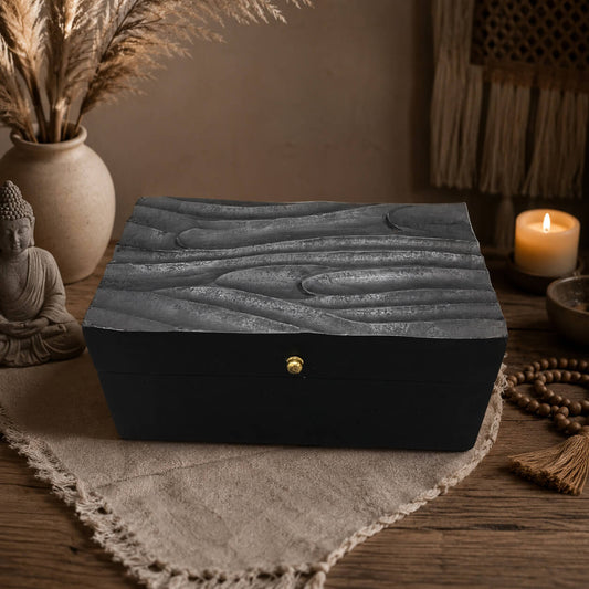 Boîte à bijoux noire en bois avec couvercle sculpté façon vagues et fermoir doré.