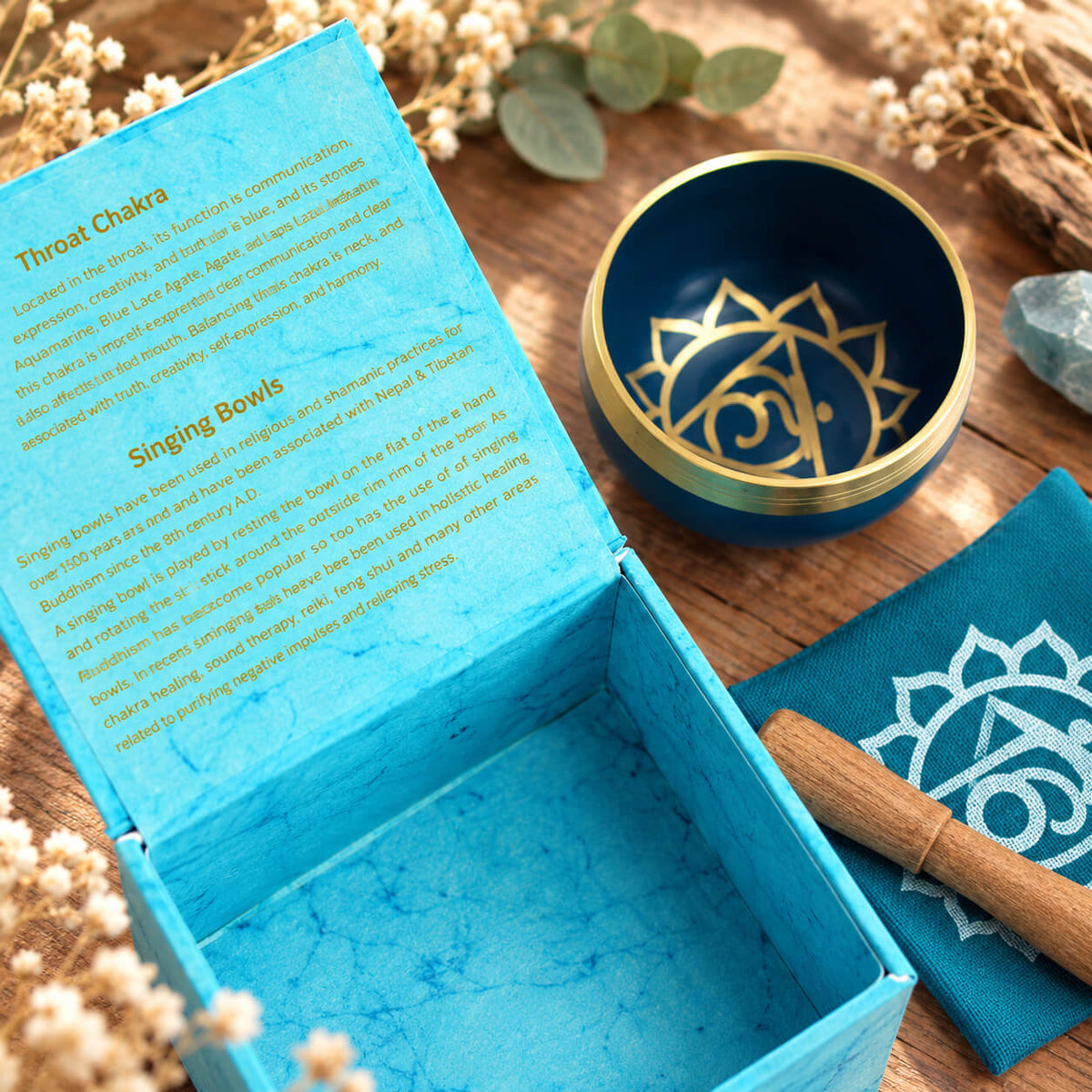 Symbole doré du chakra de la gorge au fond du bol bleu, près de la boîte turquoise ouverte et du coussin imprimé