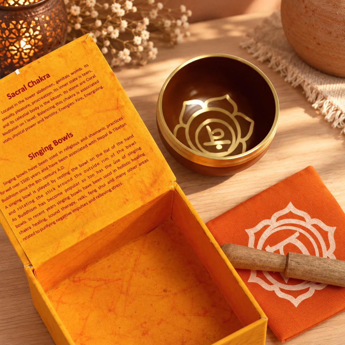 Symbole doré du chakra sacré au fond du bol orange cuivré, à côté de la boîte safran ouverte et du coussin orange