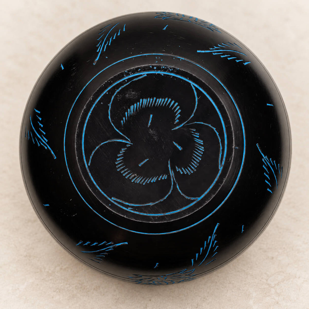 Dessous du bol chaudron noir gravé en bleu d’un motif à trois branches et de brins d’herbe