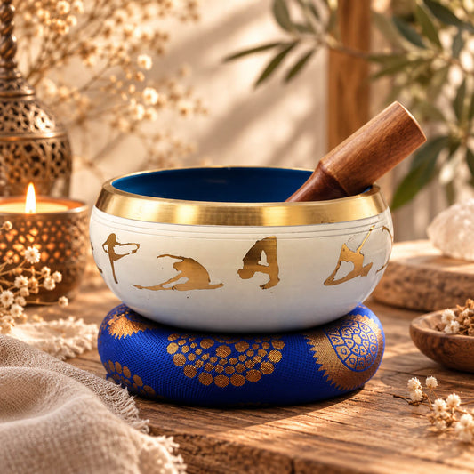 Bol chantant blanc orné de postures de yoga dorées, posé sur son coussin bleu roi avec son bâton en bois