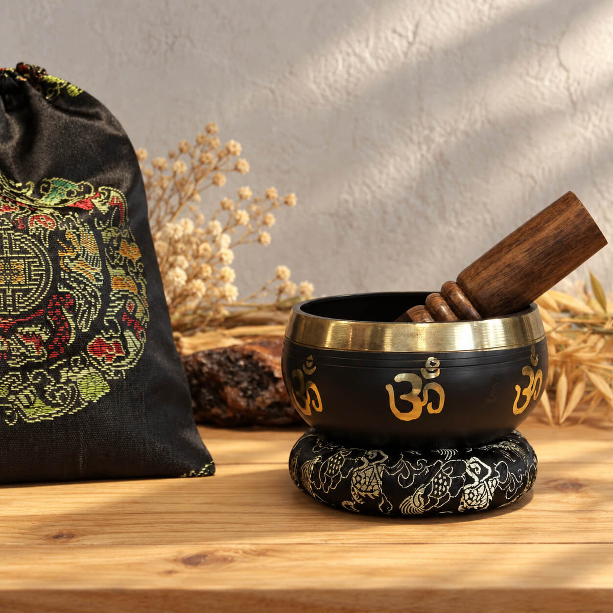 Bol chantant Om sur son coussin noir brodé, à côté de son sac à cordon orné d'une rosace