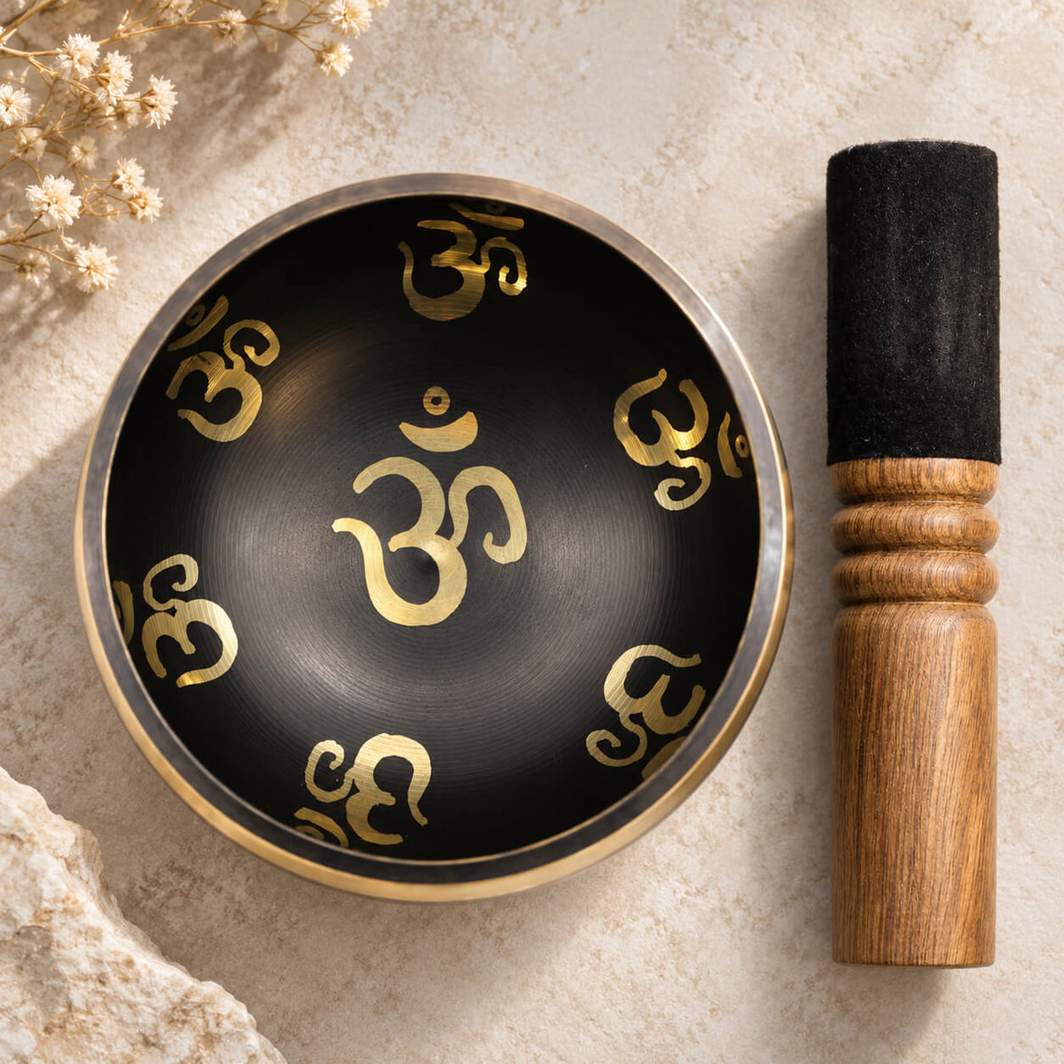 Intérieur noir du bol chantant Om, avec un grand Om doré au centre et son bâton en bois à côté
