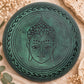 Dessous du bol chantant vert gravé d’un visage de Bouddha cerclé d’une bordure ondulée