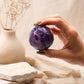 Boule d'améthyste violette à facettes tenue entre les doigts