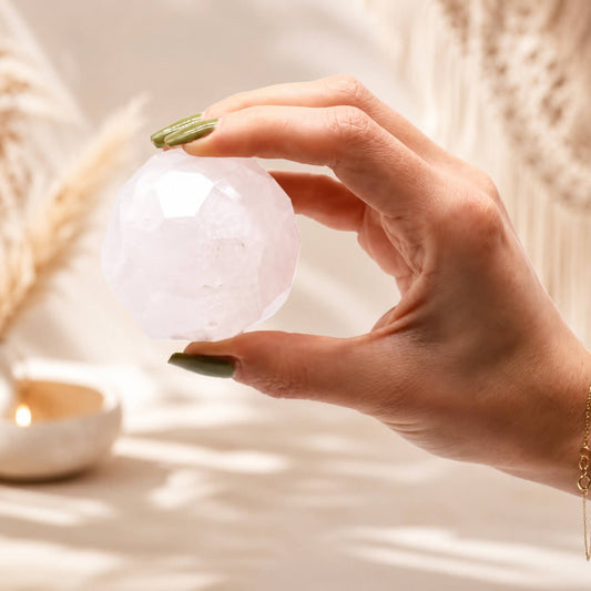 Boule de cristal de roche à facettes tenue entre les doigts