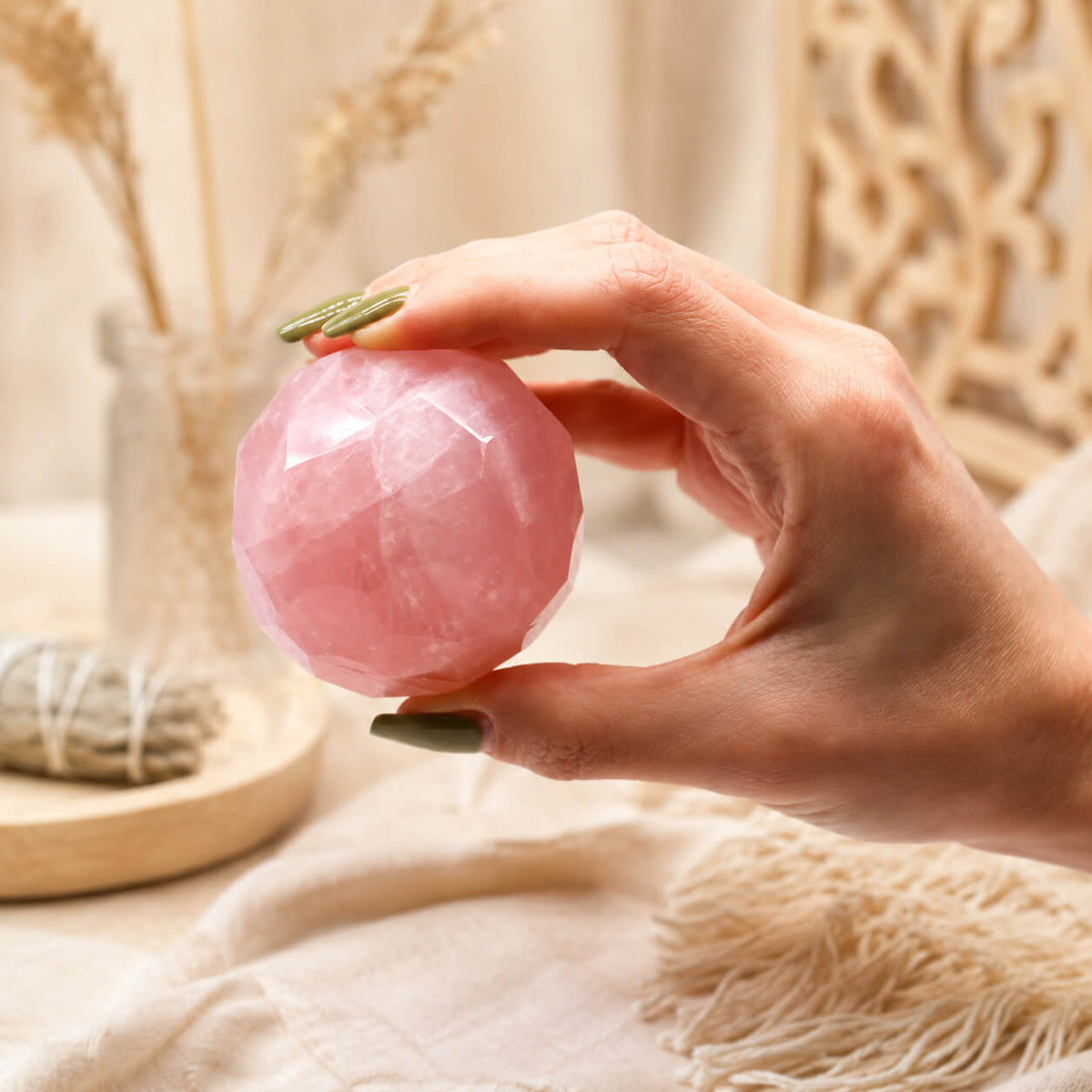 Boule de quartz rose à facettes tenue entre les doigts