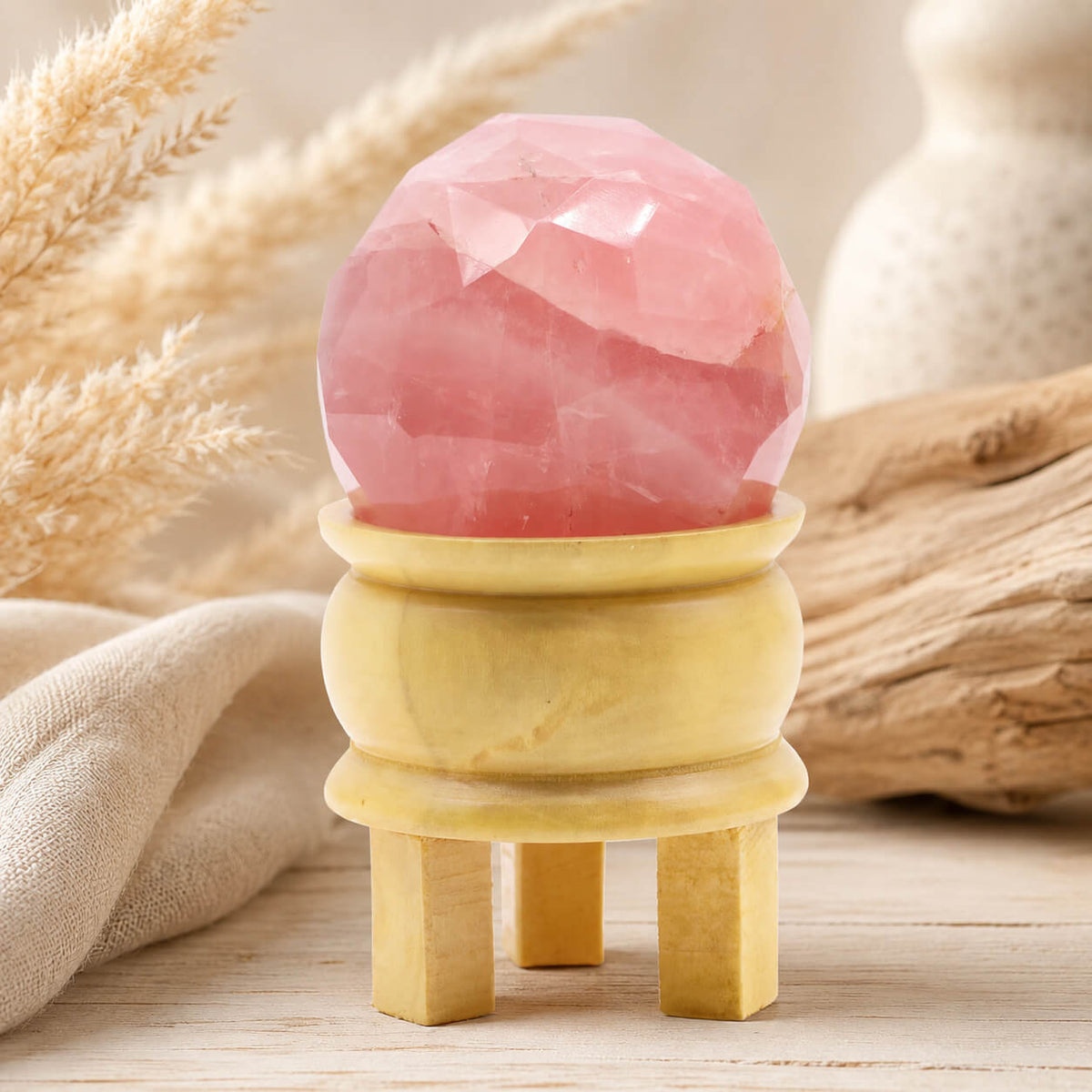 Boule de quartz rose à facettes posée sur son support tripode en bois
