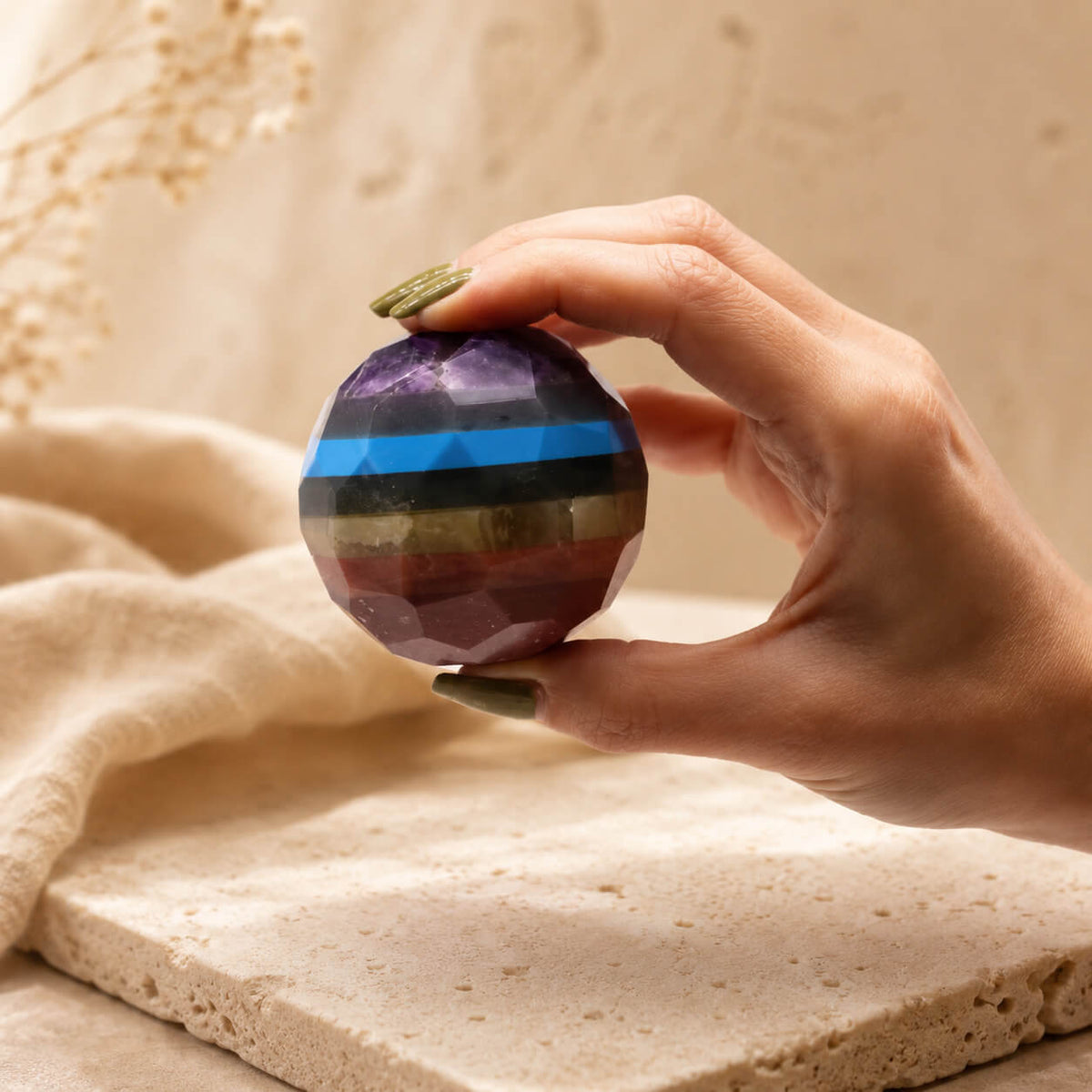 Boule des sept chakras à facettes multicolores tenue entre les doigts