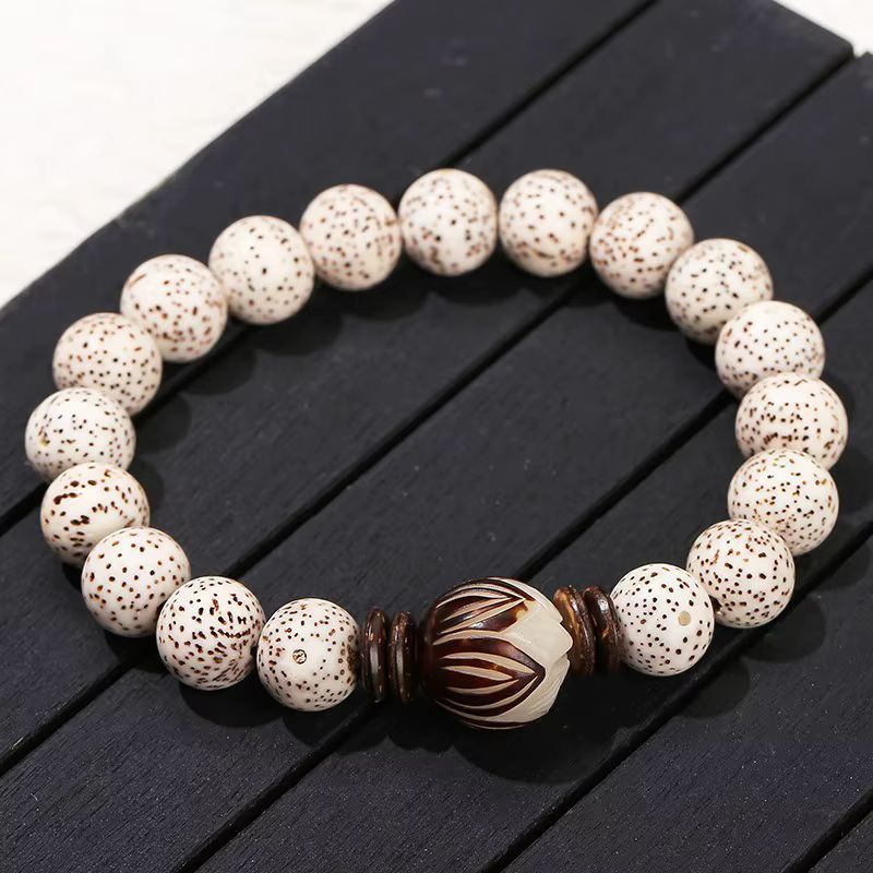 Bracelet Bodhi blanc tacheté avec lotus sculpté et anneaux en bois foncé sur fond noir.