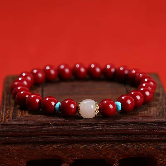 Bracelet cinabre rouge sur support en bois foncé, montrant la perle de quartz rose et les détails dorés.