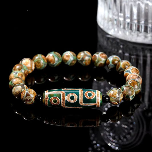 Bracelet avec perle Dzi tibétaine verte centrale ornée de motifs dorés et perles d'agate marbrées sur fond noir.