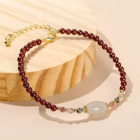 Bracelet en grenat rouge avec perle de jade centrale sur support en bois.