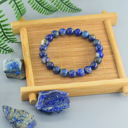 Bracelet en lapis lazuli bleu profond présenté sur support en bambou avec pierres brutes