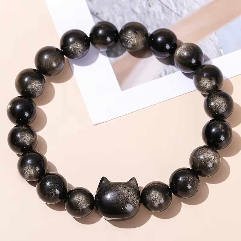 Bracelet obsidienne noire grade 7A aux reflets argentés, perles 8mm et perle décorative chat, présenté sur fond géométrique beige.