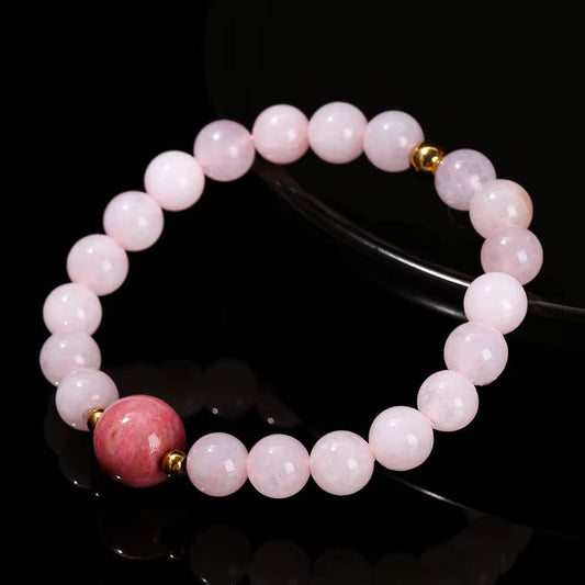 Bracelet en perles de quartz rose pâle avec une perle centrale de rhodonite rose foncé, rehaussé de détails dorés sur fond noir.