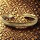 Bracelet tibétain en laiton avec gravures chevrons, photographié sur tissu ancien aux motifs géométriques dorés.