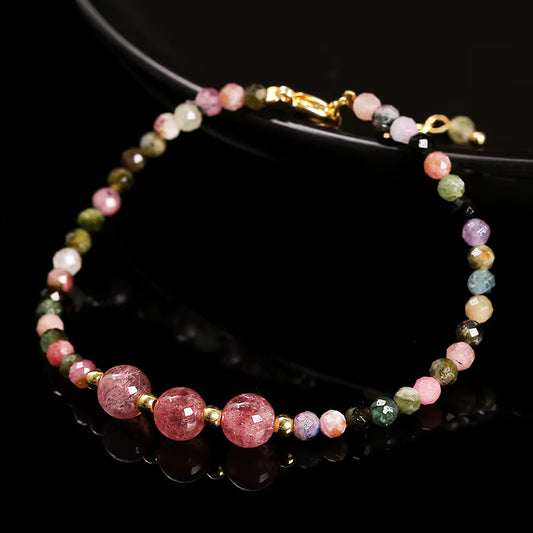 Bracelet en perles fines de tourmaline multicolore avec trois perles centrales roses plus importantes, séparées par des intercalaires dorés, sur fond noir.