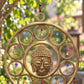 Gros plan sur le visage de Bouddha sculpté au centre du carillon mandala en laiton, clochettes dorées
