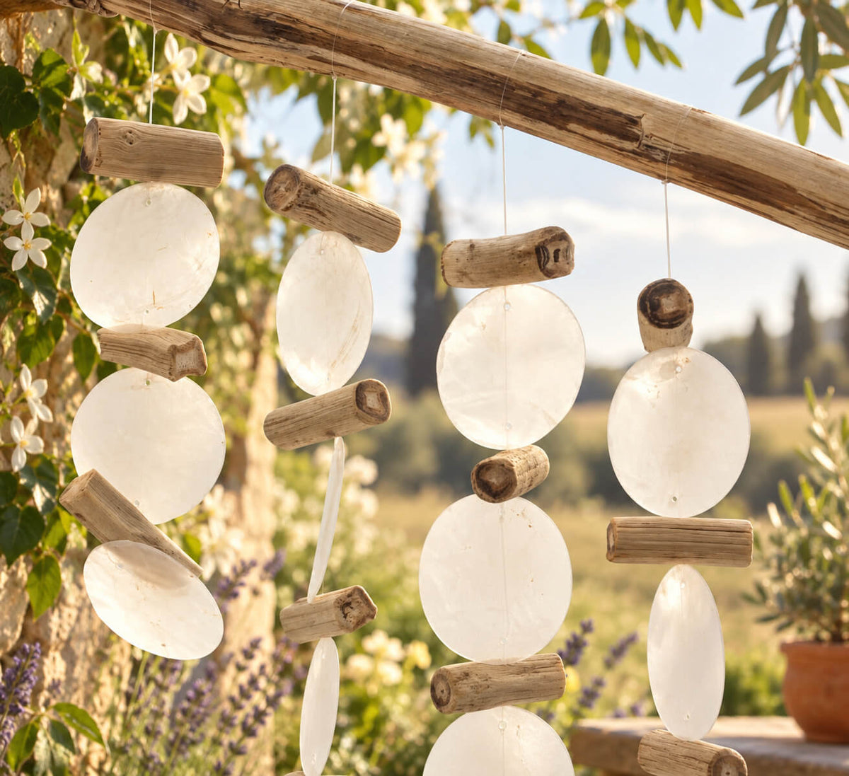 Gros plan sur les disques nacrés blancs et les brindilles de bois flotté du carillon, ambiance jardin provençal