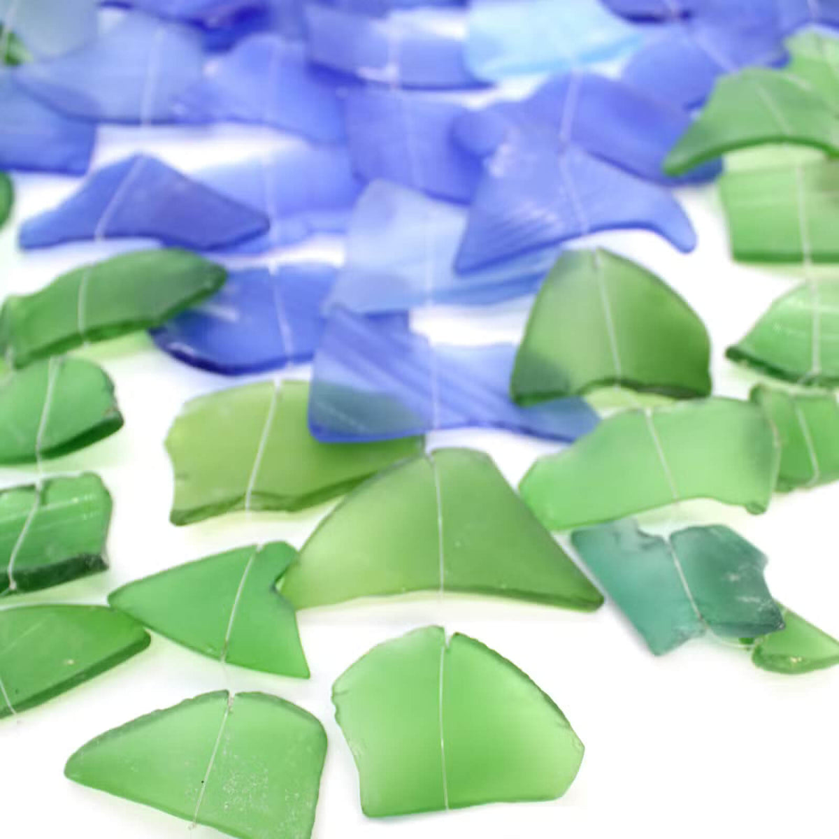 Gros plan sur les éclats de verre recyclé bleu et vert du carillon à vent, texture dépolie façon verre de mer