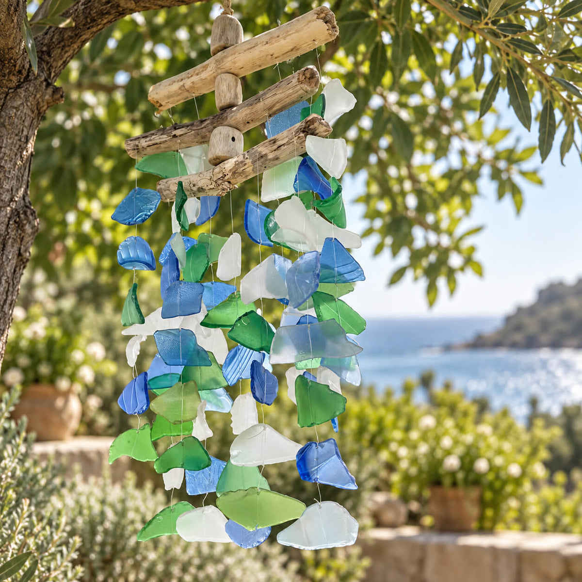 Vue rapprochée du carillon en verre recyclé multicolore, éclats bleus, verts et blancs suspendus au bois flotté